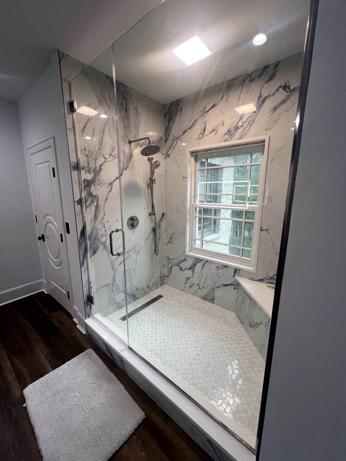 Walk-in shower with glass panels, marble-look walls, and built-in bench